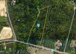 Aerial view of a wooded property outlined in yellow with a creek running through it, bordered by Charlie Stovall Rd and Thomas Greva Rd near 8438 Charlie Stovall Road, Oxford. A few houses and fields are nearby. A blue icon marked "S" is near the center.