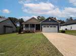 Located at 133 Ottawa Drive in Louisburg, this single-story blue house with white trim features a welcoming front porch and a spacious two-car garage. The home sits on a neatly mowed lawn with a concrete driveway, flanked by neighboring houses on either side under a partly cloudy sky.