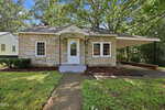 Charming single-story house with a stone exterior, small covered front porch, white door, two front windows, and an attached carport on the right. Located at 221 Zollicoffer Avenue in Henderson, the property features a yard with green grass and mature trees in the background.