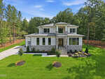 Two-story modern house with stone and white siding, large windows, a covered entryway, and landscaped front yard at 20 Cherry Bark Drive. Surrounded by green grass, small trees, and wooded areas under a blue sky with light clouds in serene Youngsville.