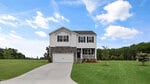 A two-story house with white siding and stone accents, located at 20 Grazing Crop Court in Youngsville, features a two-car garage and a covered front porch. The home is centered on a large green lawn with a driveway and trees in the background under a partly cloudy sky.
