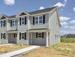 A newly built two-story townhouse at 1201 Brookrun Drive, Oxford, featuring gray siding, black shutters, and white trim. The house is situated on a corner lot with unfinished landscaping and a clear blue sky in the background.