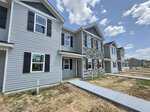 Row of newly constructed two-story townhomes with gray siding and stone accents line 1204 Brookrun Drive in Oxford. Sidewalks and small lawns are visible, with unfinished landscaping and a partly cloudy sky overhead.
