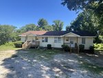 Single-story house at 413-415 Gay Street, Henderson, with a brown roof, light-colored siding, and two small front porches. The yard features patches of grass and gravel and is surrounded by trees. The sky is clear and blue.
