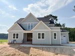Two-story modern farmhouse at 215 Broadleaf Lane, Youngsville, featuring gray board and batten siding, a black roof, white trim, multiple front-facing gables, a single-car garage, and a concrete walkway. Signs are placed near the front steps.