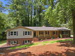 Charming single-story house at 2912 Oxford Road, Henderson, featuring a classic brick and beige siding exterior with dark shutters and a gabled roof. The inviting front porch with steps is surrounded by mature trees, fresh mulch, and a lush grassy lawn under a sunny sky.