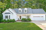 Charming single-story white house with gray roof, two dormer windows, and an attached two-car garage located at 25 Allyson Court in Youngsville. Enjoy a manicured lawn, small front porch with brick steps, and landscaped bushes. Surrounded by trees and set in a quiet residential neighborhood.