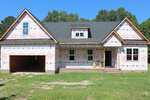 A partially constructed house at 20 Home Place Lane in Zebulon features visible roof shingles, an attached garage, and exterior walls covered in weather-resistant sheeting. There are no windows or doors installed yet, and the front yard has grass and dirt patches.