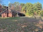 A brick house with a sloped roof sits amid trees and a grassy yard covered in scattered leaves, under a clear blue sky at 3350 Tungsten Mine Road in Bullock.