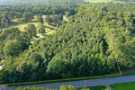Aerial view of a densely wooded 5.25-acre plot of land on Timberlake Road in Louisburg, outlined in yellow, bordered by a road in the foreground and surrounded by trees and fields in the background.