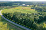 Aerial view of a large, grassy and partially wooded lot on 14 Acres Timberlake Road, Louisburg, bordered by yellow lines, with two roads curving along its edge and a building visible in the background surrounded by trees.
