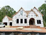 A large two-story house under construction at 300 Ironwood Boulevard, Youngsville, is covered in protective house wrap with visible branding. Bricks, construction materials, and a white van sit in front of the property, which is surrounded by trees and temporary fencing.