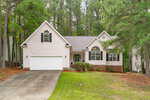 Charming single-story house at 2772 Clifton Avenue in Creedmoor featuring light siding, black shutters, a two-car garage, arched windows, and a well-maintained front lawn. The home is surrounded by tall pine trees and bordered by neighboring residences, with a concrete driveway leading directly to the spacious garage.