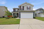 Two-story gray house with white trim and red shutters, attached two-car garage, wide driveway, green lawn, and minimal landscaping under a clear blue sky. Nestled on 50 Purple Aster Street in Youngsville, neighboring houses are visible on both sides.