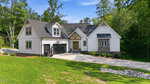 Modern two-story house at 683 Sagamore Drive in Louisburg with white siding, dark roof, black garage door, stone accents, and a welcoming front porch. Concrete driveway and landscaped lawn with shrubs enhance the curb appeal. Trees and greenery surround the property under a clear blue sky.