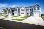 A row of modern two-story townhouses with attached garages and driveways, each painted in shades of gray, white, and blue, sits along a clean street under a clear blue sky in the heart of Youngsville. Among them is 240 Chili Rose Trail, perfectly blending comfort and contemporary style.
