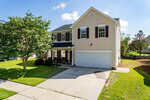 Charming two-story beige house with white trim, dark shutters, and a double garage located at 1320 Marbank Street in Wake Forest. A covered porch with chairs sits to the left of the garage. The yard is grass with a few trees, and the driveway is concrete.