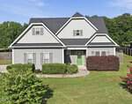 A two-story gray house with white trim, a black roof, and a green front door sits at 420 Williams-White Road in Zebulon. There are trimmed bushes, a concrete walkway, and a grassy yard, with trees and a wooden fence in the background.