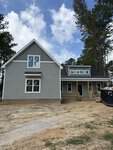 A newly constructed two-story house at 55 Copper Penny Road in Zebulon, featuring gray siding, white trim, and a covered front porch. The yard is unfinished with exposed dirt, while trees and a partly cloudy sky form the backdrop.