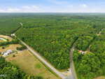 Aerial view of a rural landscape near Oxford, with dense forest, intersecting paved roads including Hwy 49 Road N, a small white house with a red roof, open fields, and several parked vehicles. The sky is partly cloudy.