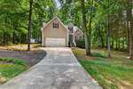 A beige two-story house with a double garage sits among tall trees at 4107 Maynard Circle in Franklinton. A concrete driveway leads to the home, and steps go up to the front entrance. The yard is green with grass and shaded by trees.