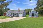 A light blue house with a front porch and attached chimney sits beside a matching detached garage, both with white trim, at 147 Bridle Trail in Youngsville. The property features a large driveway, green lawn, and trees under a blue sky.