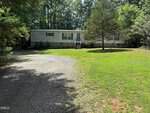 A single-story manufactured home with white siding and a small porch, surrounded by trees and greenery, is nestled at 45 Robin Lane in Henderson. A gravel driveway curves toward the house, which sits on a grassy, partially shaded lot.