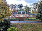 A two-story brick house with a mansard roof, central front steps, and two chimneys stands at 1909 Parker Lane in Henderson. The home is surrounded by trees and shrubbery, with a paved driveway in front and a detached garage to the left.
