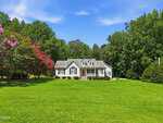 A white, single-story house with dormer windows sits on a large green lawn at 7581 NC 96 in Franklinton, surrounded by trees and flowering shrubs under a partly cloudy blue sky.