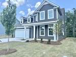 A two-story gray house with white trim, a covered front porch, attached two-car garage, and newly planted trees and shrubs, situated on a grassy lawn under a partly cloudy sky in the charming neighborhood of Franklinton at 205 Sugar Pine Drive.