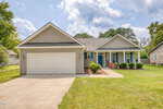 Charming single-story house at 108 Bullock Street in Franklinton, featuring gray siding, white trim, and a two-car garage. A blue front door welcomes you to a small front porch with a brick column, surrounded by a green lawn and a paved driveway under a partly cloudy sky.
