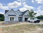 A newly constructed two-story gray house with white trim and stone accent stands at 35 Torrent Lane in Zebulon. Featuring a front porch, open garage, and a white van parked in the driveway, this property offers modern curb appeal. The yard remains unfinished, with patches of grass and dirt awaiting landscaping.