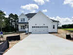 A newly constructed two-story white house at 10 Diamond Creek Drive, Zebulon, featuring a covered porch, double garage, and a wide concrete driveway. There are trees in the background and a for-sale sign on the left side of the property.