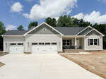 Single-story house at 55 Kettle Creek Drive in Zebulon featuring three white garage doors, a gray shingle roof, light-colored siding, a covered front porch with stone pillars, and a wide concrete driveway. Trees and partly cloudy sky are in the background.