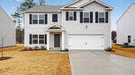 This charming two-story white house at 75 Richmond Run, Stem features black shutters and a gray front door. An attached two-car garage opens onto a concrete driveway, complemented by a small porch. The yard has dry yellow grass and minimal landscaping, with similar neighboring houses visible on both sides.