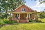 A red brick house with a covered front porch, steps leading up to the entry, and two windows above the porch sits at 3795 Graham Sherron Road in Wake Forest, surrounded by grass, trees, and plants on a sunny day.