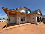 A two-story house under construction at 80 Moon Flower Walk in Youngsville features exposed plywood, window and door openings, and a covered front porch. The ground is bare reddish dirt and the sky is clear and blue.