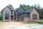 Two-story modern house at 10 Geranium Drive, Youngsville, featuring a mix of red brick and dark siding exterior, large windows, and a sloped roof. The yard is unlandscaped with patches of dirt and grass. Pine trees are visible in the background.