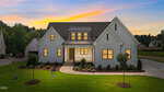 A modern white house with black-trimmed windows, a front porch, and a manicured lawn at sunset stands gracefully at 35 Firefly Lane in Louisburg. The house features peaked roofs, landscaped bushes, and a driveway, while another house is partially visible to the left.