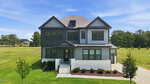 Two-story modern house with gray and white exterior, dark trim, front porch, and attached garage, situated on a grassy lot with a few young trees and a concrete driveway at 45 Scotland Drive in Youngsville. Blue sky and trees in the background.