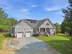 A gray house with white trim, a covered front porch, two-car garage, solar panels on the roof, and a gravel driveway sits at 665 Walnut Grove Road in Oxford, surrounded by a grassy yard and tall trees under a blue sky.