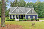 A two-story blue house with gray roof, three dormer windows, and a covered front porch, surrounded by bushes and trees at 321 Hedrick Drive. A large lawn and driveway are visible in the foreground of this charming Henderson residence.