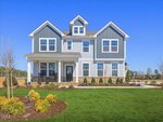 Two-story suburban house at 124 Tillamook Lane, Franklinton, featuring blue and white siding, multiple gables, and a covered front porch. The lawn is neatly manicured with shrubs and small trees, all set under a clear blue sky.