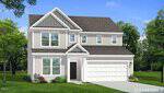 A two-story suburban house at 128 Tillamook Lane, Franklinton, featuring beige siding, white trim, a covered front entrance, and a spacious two-car garage. Large windows grace both floors. The front lawn is adorned with small shrubs and flowers, while mature trees provide a scenic backdrop.