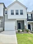 This charming two-story townhouse at 228 Alberta Drive, Franklinton features gray and white siding, three upper windows, a single-car garage, a black front door, and a small landscaped front yard with lush green grass and neatly trimmed bushes.