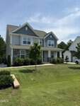Two-story suburban house with blue siding, stone accents, white trim, and a covered front porch, located at 165 Ironwood Boulevard in Youngsville. The house features a well-kept lawn, young trees, a small garden bed, and a driveway with a white vehicle parked nearby.