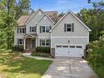 Two-story house with gray siding, white trim, and brick accents; features a double garage, front steps, and a landscaped yard with trees and shrubs under a blue sky. Nestled in Franklinton at 1708 Ripple Court, this inviting home offers both charm and comfort in a welcoming neighborhood setting.