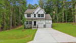 Two-story suburban house with white siding, gray stone accents, a covered front porch, and a double garage located at 100 Chanute Circle in Louisburg. Concrete driveway and well-kept lawn; the home is surrounded by tall trees and dense greenery.