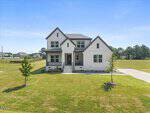 Located at 35 Scotland Drive in Youngsville, this two-story white house with dark trim features a covered front porch and a neatly landscaped yard. A concrete driveway runs along the right side, and the property is surrounded by an open grassy field with trees in the background.