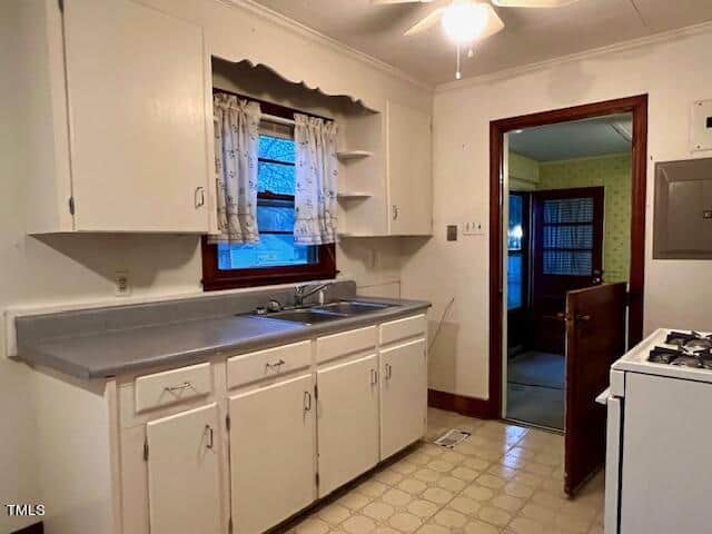 An older, dated kitchen with white cabinetry and a patterned linoleum floor.